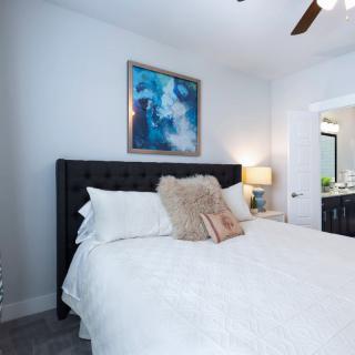 A cozy bedroom with a neatly made bed, adorned with cushions and a modern artwork above the headboard.