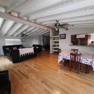 A spacious open-plan living and dining area with wooden floors, black sofas, and exposed ceiling beams.