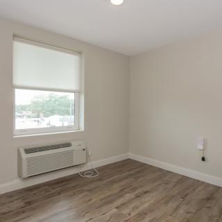 An empty room with a window, air conditioner, and hardwood flooring.