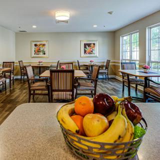 A cozy dining area featuring a bowl of fresh fruits on the table, surrounded by neatly arranged tables and chairs.
