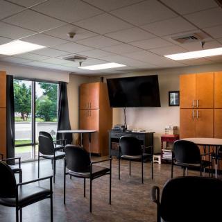 A spacious meeting room with chairs arranged around tables, featuring a large television and cabinets.