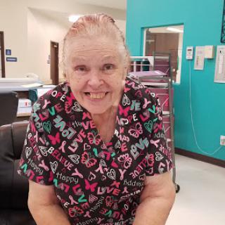 A cheerful woman in colorful scrubs poses with a smile, embodying the spirit of care and compassion in a healthcare setting.