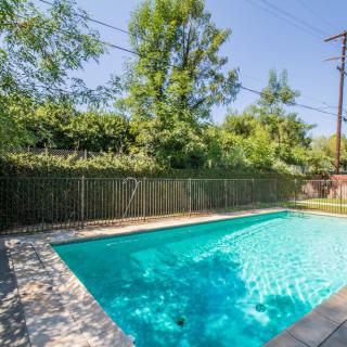 A backyard swimming pool with clear water, surrounded by trees and a wooden fence on a sunny day.