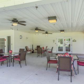 An outdoor patio with multiple tables and chairs under a covered roof, featuring ceiling fans for comfort.