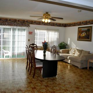 A spacious dining and living area with a table, chairs, and a sofa, illuminated by natural light from large windows.