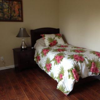 A cozy bedroom with a single bed dressed in floral bedding, accompanied by a nightstand and lamp on hardwood flooring.