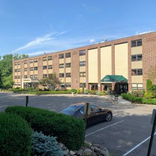 A well-maintained commercial building with a spacious parking lot and green landscaping under a clear blue sky.