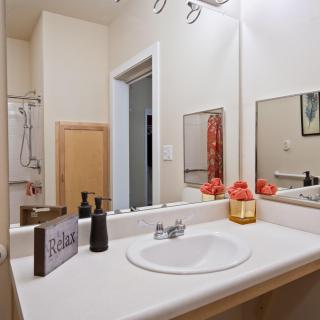 A clean and tidy bathroom with a sink, mirror, soap dispenser, and neatly arranged towels.