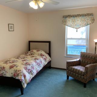 A cozy bedroom with a single bed, floral bedding, and an armchair by the window.