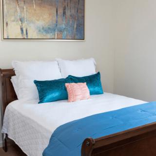 A neatly arranged bedroom with colorful pillows and a decorative painting on the wall.