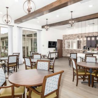 A modern dining area with wooden tables and chairs, featuring ceiling lights and large windows.
