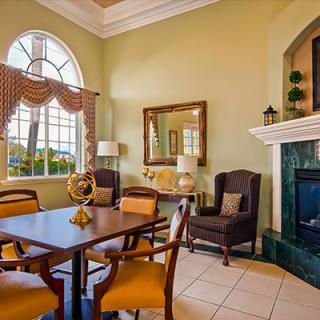 A elegantly decorated living room featuring a dining table and chairs, a cozy armchair by the fireplace, large windows, and tasteful decor.