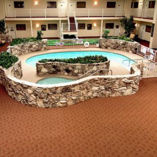 An indoor swimming pool area within a hotel atrium, featuring stone accents and lush greenery.