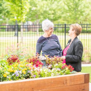 Two people having a conversation in a garden with colorful flowers.