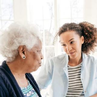A young woman shares a meaningful conversation with an elderly lady, offering emotional support in a warm indoor setting.
