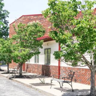 A building with a brick facade is lined with trees and benches along the sidewalk.