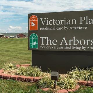 Sign for Victorian Place and The Arbors assisted living facilities with a grassy landscape in the background.