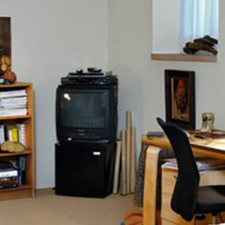 A cozy office space with a desk, chair, bookshelf, and television.