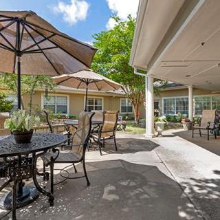 A sunny patio with tables, chairs, and umbrellas in a garden setting.