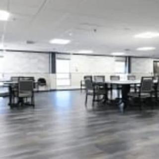A modern dining area with tables and chairs, featuring a wooden floor and bright lighting.