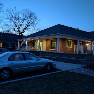 A cozy house illuminated in the early evening with a parked car nearby.
