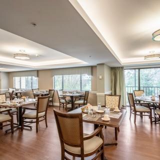 A spacious and elegantly designed dining area with neatly arranged tables and chairs, surrounded by large windows allowing natural light to brighten the space.