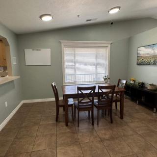 A cozy dining area with a wooden table and chairs, featuring a large window and tasteful artwork on the walls.