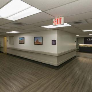 A hospital corridor with artwork on the walls and an exit sign overhead.
