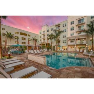 A luxurious hotel pool area with lounge chairs and palm trees at sunset.