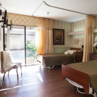 A hospital room with two patient beds, a chair, and a large window allowing natural light to enter.