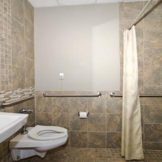 A modern bathroom with tiled walls, featuring a toilet, sink, and shower area with curtain and handrails.