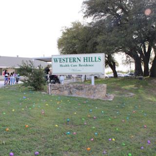 A sign for Western Hills, situated in a grassy area with trees nearby.