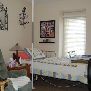 A cozy bedroom with a hospital bed and home care setup, featuring a comfortable chair and decorative elements.