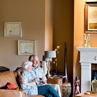 An older couple sitting together on a couch in a warmly decorated living room.