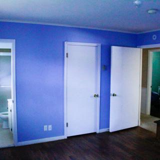 A room with blue walls, white doors, and dark wood flooring, featuring a view into an adjacent bathroom.