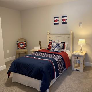 A cozy bedroom with a single bed featuring striped bedding, a nightstand with a lamp, and simple decor.