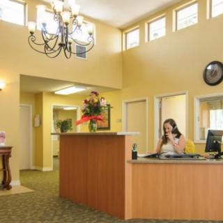 A receptionist working at a desk in a well-lit office lobby with a chandelier and floral arrangement.