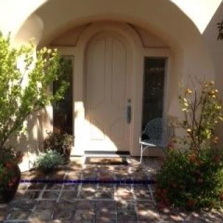 An arched doorway surrounded by potted plants, casting shadows on the entrance.