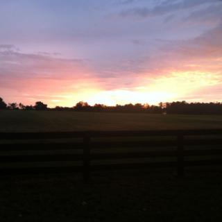 A beautiful sunset over a quiet field with a silhouetted fence in the foreground.