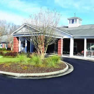 A welcoming residential building with a curved driveway surrounded by greenery under a partly cloudy sky.