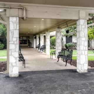 A covered walkway with stone pillars and benches along the sides, surrounded by greenery.