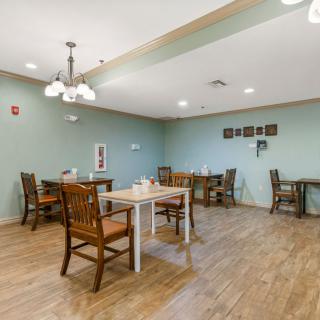 An empty dining room with wooden tables and chairs, featuring soft lighting and simple wall decor.