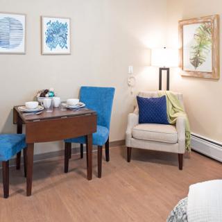 A cozy living and dining area with a small table, chairs, and artwork on the walls.
