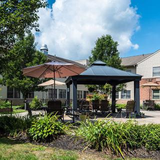 A serene outdoor patio area with a gazebo, surrounded by lush greenery and trees under a cloudy sky.