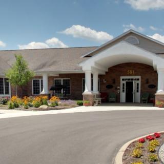 A welcoming building entrance with landscaped gardens and a circular driveway under a clear blue sky.