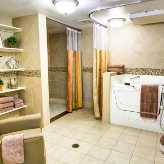 A well-equipped accessible bathroom featuring a walk-in tub and open shower area with shelves stocked with towels.