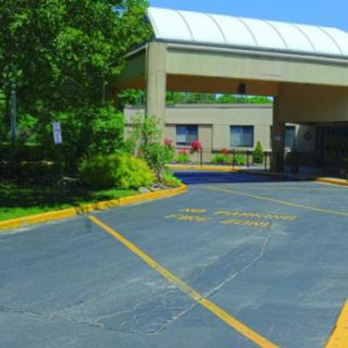 A driveway leading to a building entrance on a sunny day with trees and landscaping.