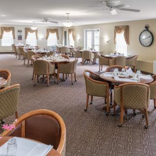 A spacious dining room with neatly arranged tables and chairs, well-lit by large windows.