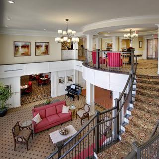 A spacious hotel lobby featuring stylish furniture, a grand staircase, and elegant chandeliers.