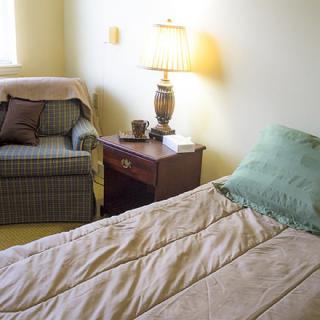 A cozy bedroom with a bed, nightstand, lamp, and an armchair.